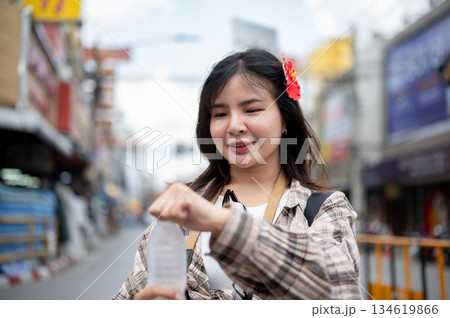 Asian tourist woman with red hibiscus flower on hair opening a water bottle to drink in local market Asian tourist woman with red hibiscus flower on hair opening a water bottle to drink in local market 134619866