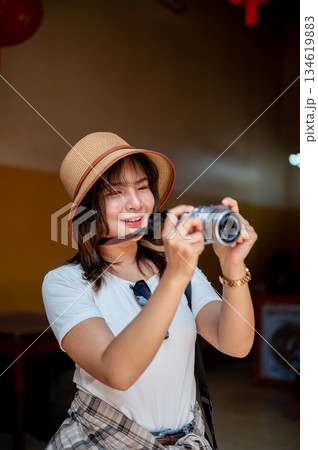 Asian woman wearing hat smiling while holding camera taking photos around the Chinese shrine temple Asian woman wearing hat smiling while holding camera taking photos around the Chinese shrine temple 134619883