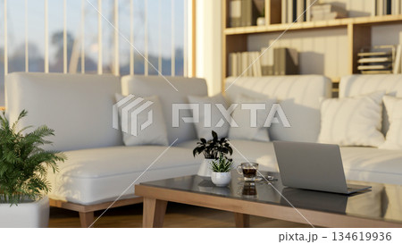 Laptop and coffee on glass top wooden table and white sofa in living room with glass wall and blinds Laptop and coffee on glass top wooden table and white sofa in living room with glass wall and blinds 134619936