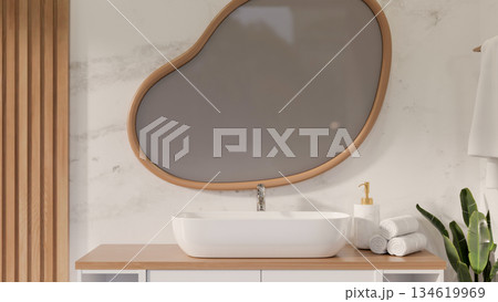 Irregular odd shape mirror hanging on shiny marble wall over a white ceramic sink with towels in a classy bathroom. Irregular odd shape mirror hanging on shiny marble wall over a white ceramic sink with towels in a classy bathroom. 134619969