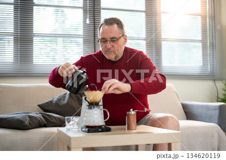 Old white man wearing glasses using kettle pouring hot water into coffee in filter paper on table. Old white man wearing glasses using kettle pouring hot water into coffee in filter paper on table. 134620119
