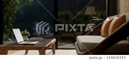 White screen laptop on table in front of a sofa or armchair in living room with glass door at night. White screen laptop on table in front of a sofa or armchair in living room with glass door at night. 134620355