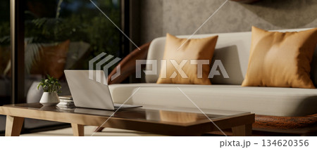 Laptop on wooden table in front of a sofa or armchair in a living room with glass doors at night. Laptop on wooden table in front of a sofa or armchair in a living room with glass doors at night. 134620356