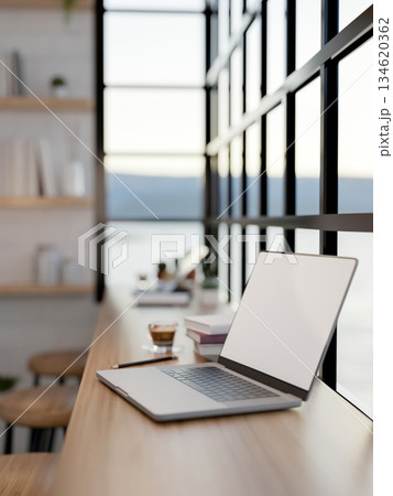 Blank screen laptop and coffee in glass cup with books on wooden table with chairs in a seaside cafe 134620362