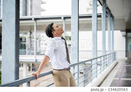 Businessman or office worker standing and leaning with both hands on pedestrian footbridge's railing 134620563