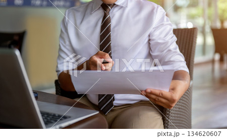 Close up of male office worker pointing at document over laptop on wood table in cafe or coffee shop Close up of male office worker pointing at document over laptop on wood table in cafe or coffee shop 134620607