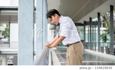 Businessman or office worker holding a railing with both hand looking down on pedestrian footbridge. Businessman or office worker holding a railing with both hand looking down on pedestrian footbridge. 134620630