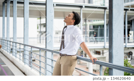 Businessman or office worker closing eyes leaning with both hands on pedestrian footbridge's railing 134620640