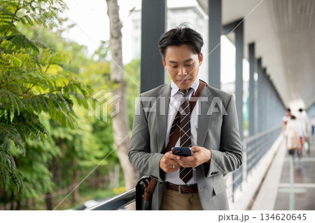 Businessman or office worker holding and looking at phone chatting with family on pedestrian footbridge. 134620645