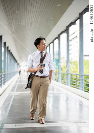 Businessman or office worker holding a phone looking around while walking on a pedestrian footbridge 134620653