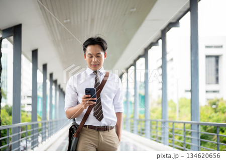 Businessman or office worker looking at phone chatting or calling while walking on a pedestrian footbridge. 134620656