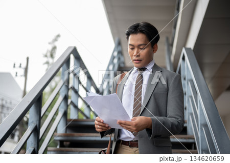 Businessman or office worker looking at document in his hands standing on flyover or overpass stairs Businessman or office worker looking at document in his hands standing on flyover or overpass stairs 134620659