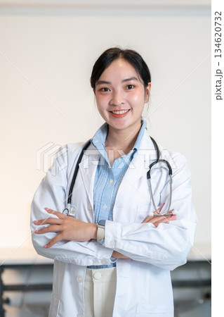 Asian female doctor with stethoscope is smiling while standing with arms crossed in a diagnosis room 134620732