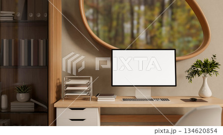 Blank screen computer on wooden table under oval window with garden scenery outside the living room. 134620854