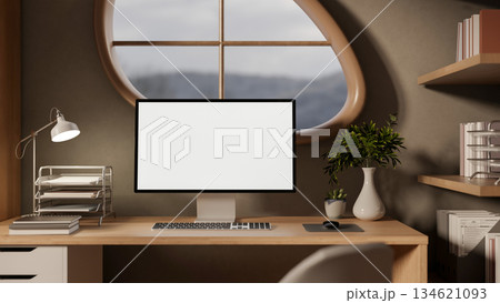 White screen computer on wooden study table aside bookshelf under oval window in a bedroom's corner 134621093