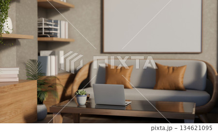 Laptop and coffee cup on glass top wooden table in front of a sofa in a cosy minimalist living room. Laptop and coffee cup on glass top wooden table in front of a sofa in a cosy minimalist living room. 134621095