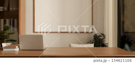 Laptop aside bonsai and book on wooden table with frame on wall aside cabinet in living room or cafe Laptop aside bonsai and book on wooden table with frame on wall aside cabinet in living room or cafe 134621108