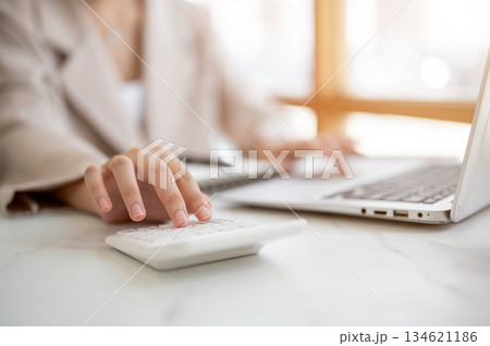 Close up of hands typing on laptop keyboard and using calculator at table aside glass wall in cafe. 134621186