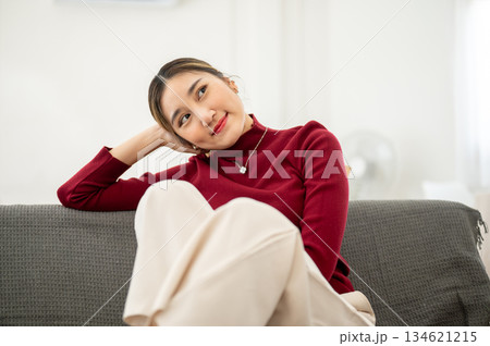 Pretty asian woman resting head on a hand while sitting legs up on fabric sofa in a living room or studio.rest 134621215