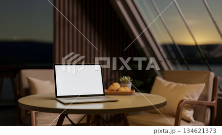 Coffee cup aside book on a round wooden table with armchair in living room or cafe under roof window 134621373