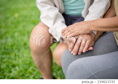 Close up of old man and woman hands with gold wedding rings clasping together while sitting in park. 134621535