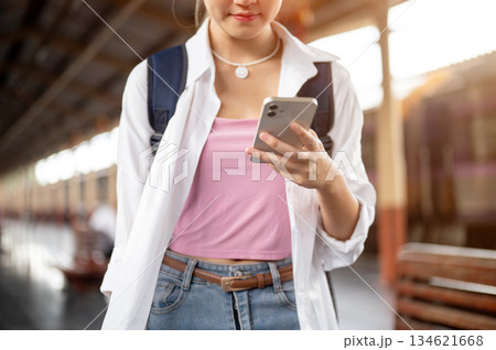 Close up woman with bag holding and looking at smartphone while standing or walking at train station Close up woman with bag holding and looking at smartphone while standing or walking at train station 134621668