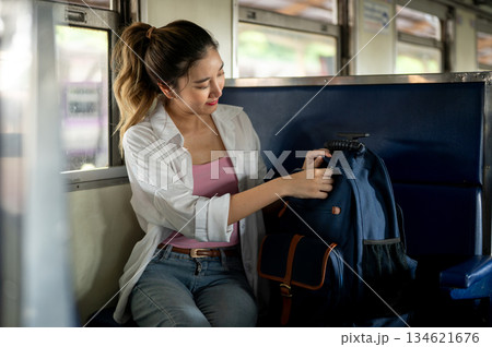 Pretty asian woman opening or zipping up blue bag while sitting on carriage bench at train station. Pretty asian woman opening or zipping up blue bag while sitting on carriage bench at train station. 134621676