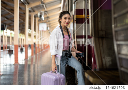Asian woman with camera holding phone and luggage as walking into carriage at train station platform Asian woman with camera holding phone and luggage as walking into carriage at train station platform 134621708
