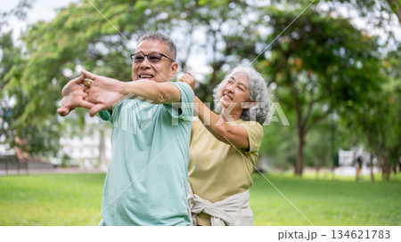 Old woman massaging glasses man shoulders while he standing and stretching on grass lawn in the park 134621783