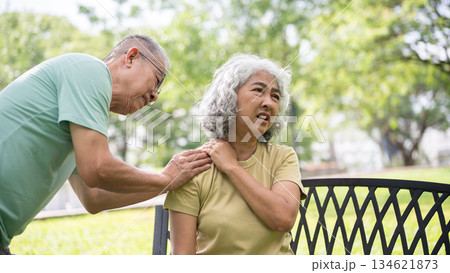 Old man holding or massaging pained or injury shoulder of woman sits on bench after workout in park. Old man holding or massaging pained or injury shoulder of woman sits on bench after workout in park. 134621873