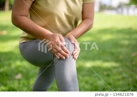 Old woman holding or massaging her pained or injury knee on bench after exercise or workout in park. Old woman holding or massaging her pained or injury knee on bench after exercise or workout in park. 134621876