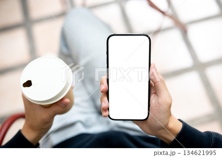 Hands holding coffee and white screen smartphone using application or social media as sits on bench. 134621995