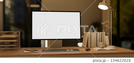 White screen computer with books and aside lamp on wooden table in a dim lit living room or bedroom. 134622028
