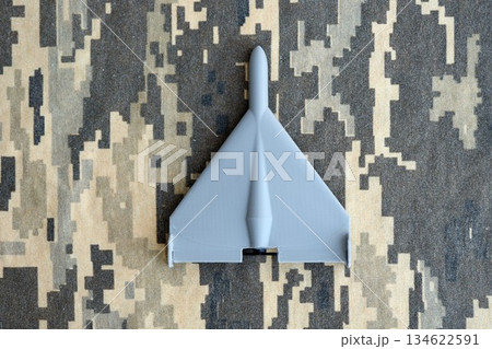 Unnamed grey toy drone model on camouflage fabric close up. Kamikaze drone for bombing targets 134622591