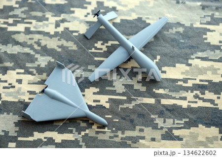 Unnamed grey toy drones models on camouflage fabric close up. Kamikaze drone and observation drone Unnamed grey toy drones models on camouflage fabric close up. Kamikaze drone and observation drone 134622602