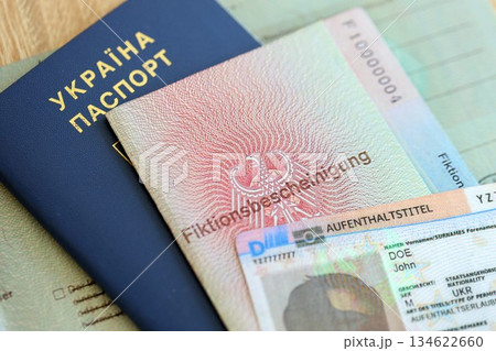 German Permanent resident card and document specimen lies with Ukrainian passport on wooden table close up. Aufenthaltstitel and Fiktionsbescheinigung German Permanent resident card and document specimen lies with Ukrainian passport on wooden table close up. Aufenthaltstitel and Fiktionsbescheinigung 134622660
