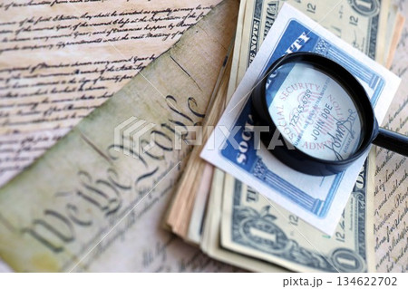 SSN Social Security Number card Under magnifying glass with dollar bills on US Constitution close up 134622702