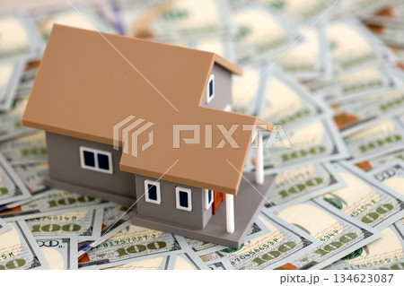 Toy house on big amount of US dollar bills close up. Real estate and building construction concept Toy house on big amount of US dollar bills close up. Real estate and building construction concept 134623087
