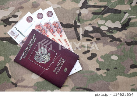 Russian passport with money on multicam camouflage fabric close up. Concept of russian army funds and invasion to Ukraine Russian passport with money on multicam camouflage fabric close up. Concept of russian army funds and invasion to Ukraine 134623654