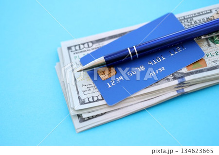 Credit card and pen with US dollar currency money bills banknotes on light blue background. Business, financial operations and accounting in United States of America Credit card and pen with US dollar currency money bills banknotes on light blue background. Business, financial operations and accounting in United States of America 134623665