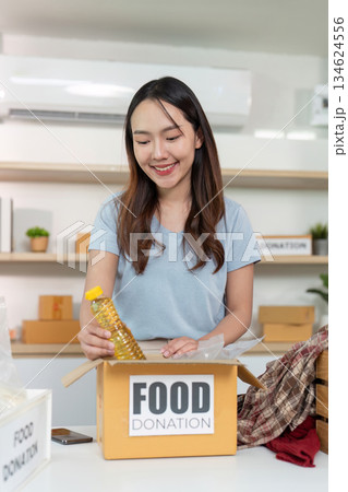 Food Donation. Woman placing cooking oil into a donation box with a smile. 134624556