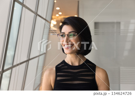 Cheerful Armenian businesswoman looks out window with joyful expression, headshot 134624726