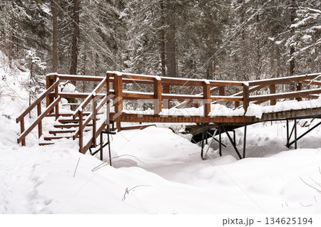 Wooden bridge over river covered with snow in forest in winter. Wooden bridge over river covered with snow in forest in winter. 134625194
