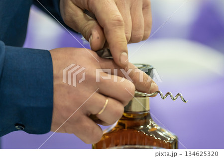 A man with a corkscrew in his hands opens a bottle of brandy. 134625320