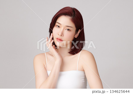 A beautiful young Asian woman with clean, fresh skin against a grey background. Skincare, facial treatment, cosmetology, beauty, and spa. An elegant portrait of an Asian woman. 134625644
