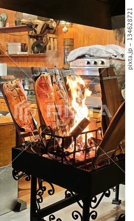 Salmon fillet smoked on wooden planks over open fire inside a traditional restaurant kitchen. The image represents authentic cooking tradition fire preparation and artisanal food culture 134628721