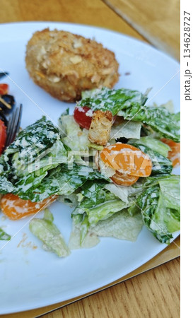 Plate with fresh Caesar style salad topped with creamy dressing, crouton, cherry tomato, and breaded cutlet on a wooden table. The image represents healthy eating, balanced meal Plate with fresh Caesar style salad topped with creamy dressing, crouton, cherry tomato, and breaded cutlet on a wooden table. The image represents healthy eating, balanced meal 134628727