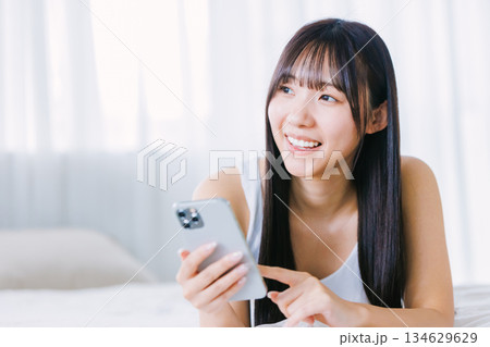 ベッドでスマホを使う若い女性 134629629