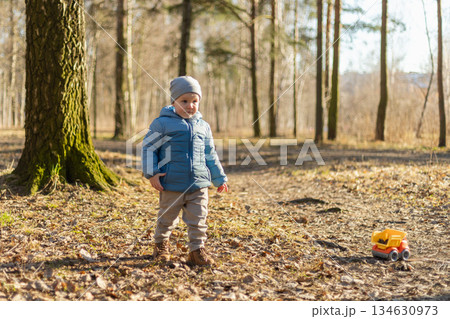 Happy baby child outdoor. Little toddler boy with toy car having fun on walk in park. Baby son smiling playing outdoor. Little child resting walking in nature. Little toddler child having fun on walk 134630973