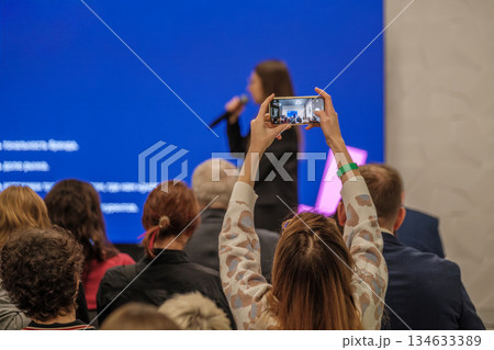Audience at conference captures speaker on stage using a smartphone during presentation Audience at conference captures speaker on stage using a smartphone during presentation 134633389